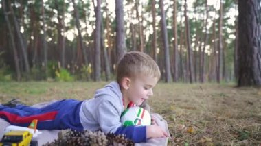 baby boy play ball in the park on sunset. Kid dream concept. kid baby play football soccer in nature park. baby kicking the ball running down fun the road in the park. Slow motion. FullHD footage