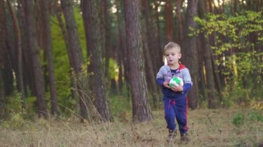 baby boy play ball in the park on sunset. Kid dream concept. kid baby play football soccer in nature park. baby kicking the ball running down fun the road in the park. Slow motion. FullHD footage