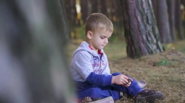 Little boy sitting in the woods playing with a fallen cone. Slow motion. High quality FullHD footage