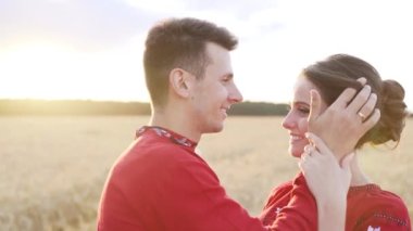 A guy is kissing a girl in a wheat field at sunset. Couple in national clothing. High quality FullHD footage