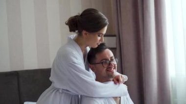 Authentic close up shot of young just married couple wearing pajamas having fun to tickling each other on the bed in the bedroom of hotel. Just woke up early in the morning in a sunny day. FullHD