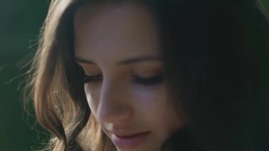 Genç utangaç kadın gölde kameraya bakıyor ve gülümsüyor. Güneş parlıyor. Ağır çekim duygusu. Yüksek kaliteli FullHD görüntüler