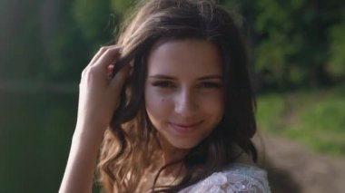 Güneş ışığında güzel bir kadının portresi. Mavi arka plan ve güneş ışınlarıyla gülümseyen kadın. Kameraya sevgiyle bakan nazik kadın portresi. Yavaş çekim.