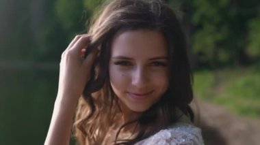 Portrait of beautiful woman in sunlight. Smiling woman face in blue sky background and sunbeams. Portrait of gentle female person looking at camera with love. Blue-eyed girl posing in sunshine outdoor