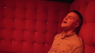 Gece kulübünün kırmızı odasında bir kanepede şarkı söyleyen genç adam. Müzik videosu çekiyoruz. Yüksek kalite 4k görüntü