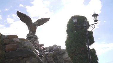 Doğal taşların üzerinde süslü bir şelale ve mavi gökyüzü kartal heykeli. Yavaş çekim düşüyor. Yüksek kaliteli FullHD görüntüler