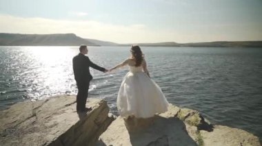 Yazın, taş kaya plajında el ele tutuşan çift, deniz kenarındaki bir plajda el ele tutuşan Asyalı sevgili çift. Suda köpüklü bokeh. Yüksek kaliteli FullHD görüntüler