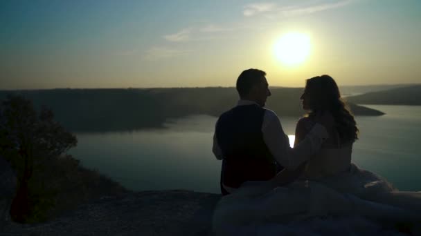 在夕阳西下的山顶上 一对恋爱中的亚洲夫妇坐在一起的轮廓 爱情伴侣在山顶上看着日落和岛屿 优质Fullhd影片 — 图库视频影像