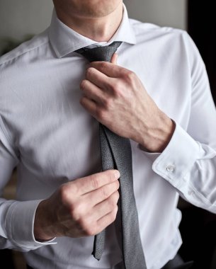 Gömlekli bir adam evde kravat takıyor.