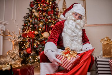 Noel Baba, çocuklara mutlu Noeller dilemek için büyük kırmızı çantasına hediyeler koyar..