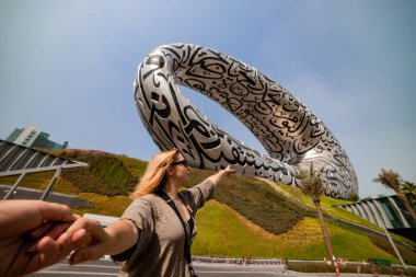 DUBAI / United Arab Emirates-8 / 11 / 2021 - Dubai şehir merkezinde ExPO 2020 için inşa edilen Geleceğin Müzesi yakınlarındaki Kadın Turist, Dış yüzeyinde Arap şiiri olan İnanılmaz Modern Mimari Tasarımı