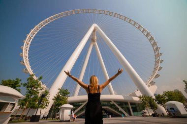 Kadın, Bluewater Adası 'ndaki dünyanın en büyük dönme dolaplarından biri olan Ain (Eye) DUBAI' yi görünce sevinçle ellerini kaldırdı. Birleşik Arap Emirlikleri 'nin en iyi turistleri arasında