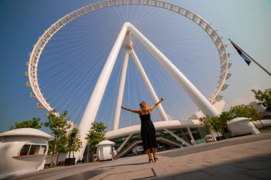 Kadın, Bluewater Adası 'ndaki dünyanın en büyük dönme dolaplarından biri olan Ain (Eye) DUBAI' yi görünce sevinçle ellerini kaldırdı. Birleşik Arap Emirlikleri 'nin en iyi turistleri arasında