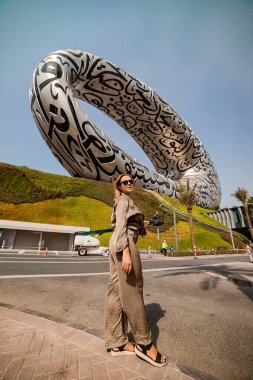 DUBAI / United Arab Emirates-8 / 11 / 2021 - Dubai şehir merkezinde ExPO 2020 için inşa edilen Geleceğin Müzesi yakınlarındaki Kadın Turist, Dış yüzeyinde Arap şiiri olan İnanılmaz Modern Mimari Tasarımı