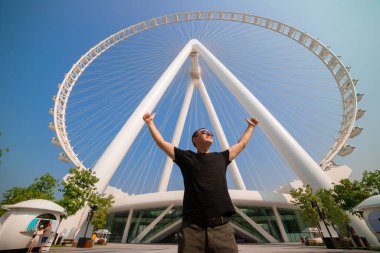 Erkek turist, dünyanın en büyük dönme dolaplarından biri olan Ain (Eye) DUBAI 'nin Bluewater adasındaki görüntüsünden zevk alarak ellerini kaldırdı. Birleşik Arap Emirlikleri 'nin en iyi turistleri arasında