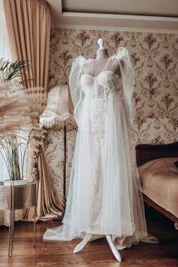 Güzel gelinlik odada asılı, kadın törenden önce hazırlanıyor.