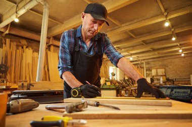 Bir ahşap ile çalışan usta bir marangozun portresi, bir kalemle tahta işaretleme ve marangozluk atölyesinde bir parça mobilya yapmak için bir parça odun kesmek için ölçümler alma