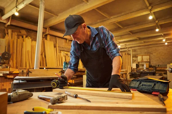 木で作業する上級大工の肖像 鉛筆で板をマーキングし 大工の工房で家具を作るために木を切るための測定 — ストック写真