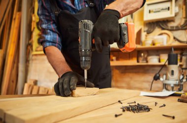 Marangozluk atölyesinde çalışan marangoz bir parça mobilya yapmak için sondaj aleti kullanıyor.