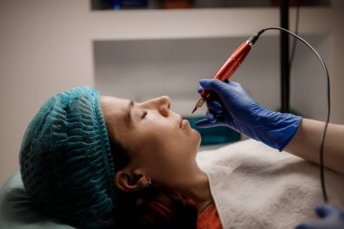 Genç kadın dövme salonu, closeup kalıcı dudak makyaj prosedürü geçiren