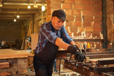 Üniformalı bir marangozun portresi marangozluk fabrikasında ahşap parmaklıkları el baskısıyla yapıştırıyor.