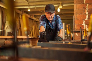 Üniformalı bir marangozun portresi marangozluk fabrikasında ahşap parmaklıkları el baskısıyla yapıştırıyor.