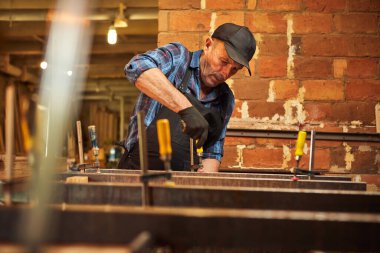 Üniformalı bir marangozun portresi marangozluk fabrikasında ahşap parmaklıkları el baskısıyla yapıştırıyor.