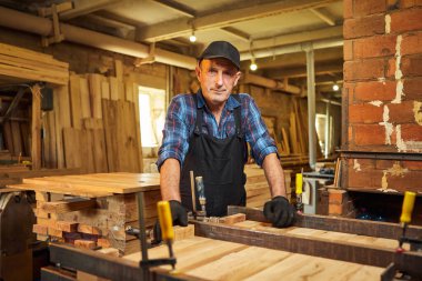 Üniformalı bir marangozun portresi marangozluk fabrikasında ahşap parmaklıkları el baskısıyla yapıştırıyor.