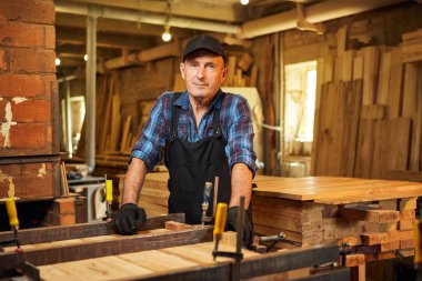 Üniformalı bir marangozun portresi marangozluk fabrikasında ahşap parmaklıkları el baskısıyla yapıştırıyor.