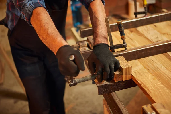 Üniformalı kıdemli marangoz marangozda el baskısıyla tahta parmaklıkları yapıştırıyor.