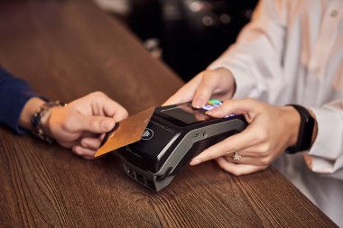 Müşterinin eli NFC teknolojisiyle temassız bir kredi kartı için ödeme yapıyor. Kredi kartı okuyucusu olan bir barmen. Ellere odaklan..