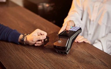 Müşterinin eli NFC teknolojisiyle temassız bir kredi kartı için ödeme yapıyor. Kredi kartı okuyucusu olan bir barmen. Ellere odaklan..