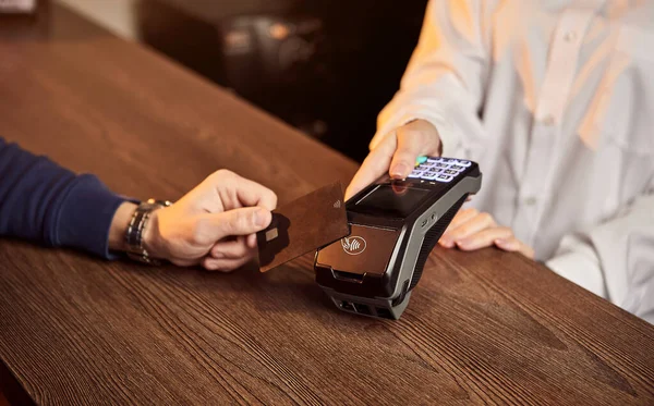 Müşterinin eli NFC teknolojisiyle temassız bir kredi kartı için ödeme yapıyor. Kredi kartı okuyucusu olan bir barmen. Ellere odaklan..