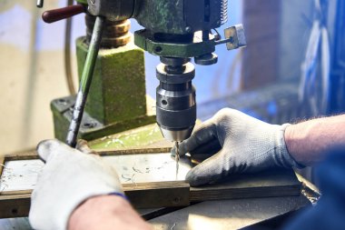 Çalışan, alüminyum düz çelik plaka ve bank matkabı sondajı yapıyor. Metal matkap kısmı endüstriyel makinede çelik bölmede delikler açıyor. Metal iş endüstrisi