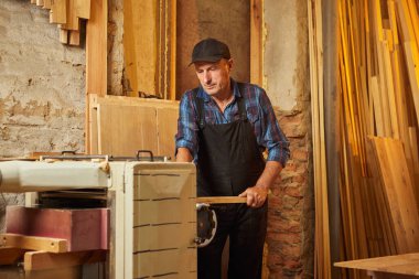 Üniformalı kıdemli marangoz marangozluk fabrikasında ahşap işçiliği yapıyor. 