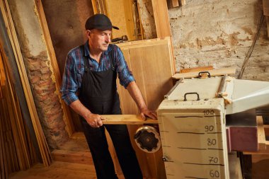 Üniformalı kıdemli marangoz marangozluk fabrikasında ahşap işçiliği yapıyor. 