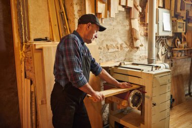 Üniformalı kıdemli marangoz marangozluk fabrikasında ahşap işçiliği yapıyor. 