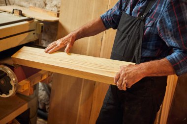 Üniformalı kıdemli marangoz marangozluk fabrikasında ahşap işçiliği yapıyor. 