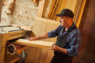 Üniformalı kıdemli marangoz marangozluk fabrikasında ahşap işçiliği yapıyor. 