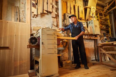 Üniformalı kıdemli marangoz marangozluk fabrikasında ahşap işçiliği yapıyor. 