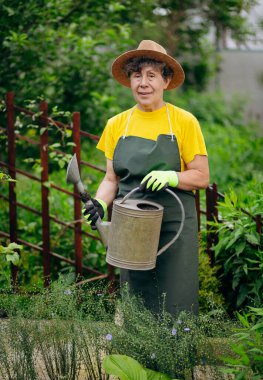 Bahçesinde iş aletleriyle çalışan şapkalı kıdemli kadın bahçıvan. Bahçe işleri, çiçek ve bitkilerle ilgilenmek ve büyümek..