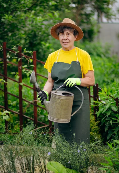 Bahçesinde iş aletleriyle çalışan şapkalı kıdemli kadın bahçıvan. Bahçe işleri, çiçek ve bitkilerle ilgilenmek ve büyümek..