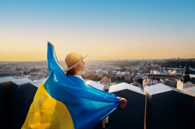 Bir kadın ulusal Ukrayna bayrağıyla duruyor ve Lviv 'de günbatımında barış için dua ediyor.