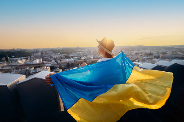 A woman stands with the national Ukrainian flag and waving it praying for peace at sunset in Lviv