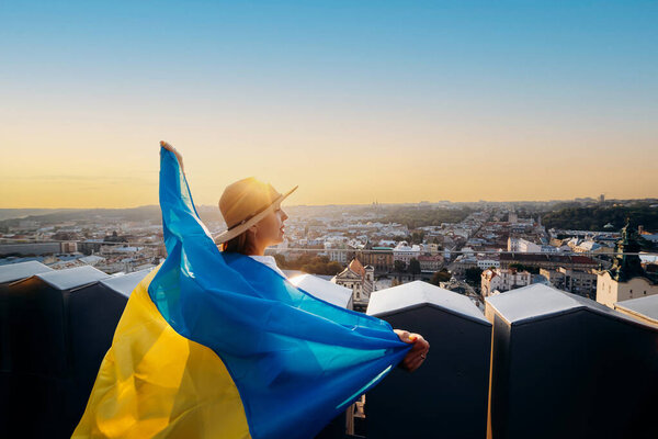 A woman stands with the national Ukrainian flag and waving it praying for peace at sunset in Lviv