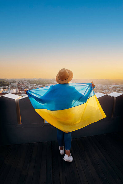 A woman stands with the national Ukrainian flag and waving it praying for peace at sunset in Lviv