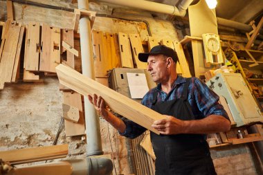 Üniformalı kıdemli marangoz marangozluk fabrikasında ahşap işçiliği yapıyor. 