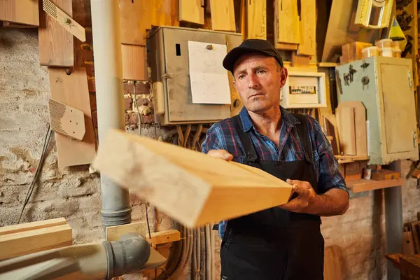 Üniformalı kıdemli marangoz marangozluk fabrikasında ahşap işçiliği yapıyor. 