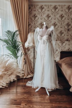 Güzel gelinlik odada asılı, kadın törenden önce hazırlanıyor.