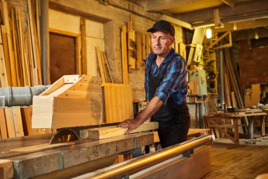 Elektrikli testere ile ahşap kesme masası. Kıdemli profesyonel marangoz üniformalı kereste fabrikasında ahşap tahta kesiyor. Testere makinesi